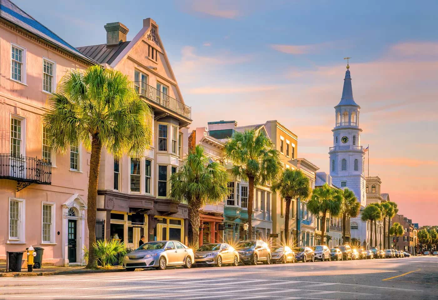 Broad Street in downtown Charleston, SC in golden evening light, palmettos and pastel storefronts leading to the St. Michael's Church steeple