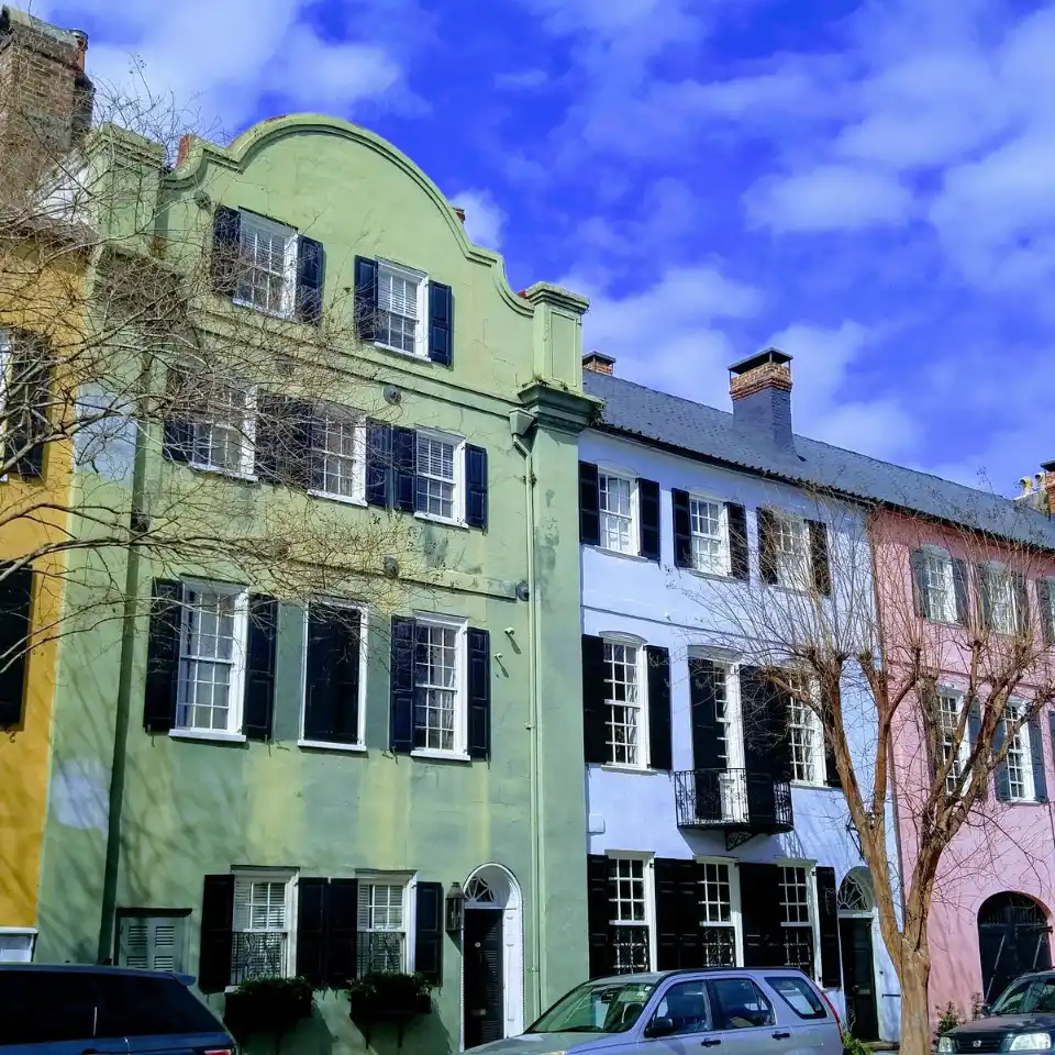 Colorful historic row houses with arched windows and contrasting shutters under a blue sky.