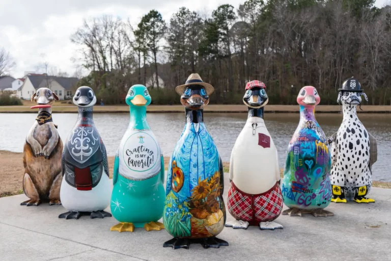 Seven colorfully decorated penguin sculptures standing by a lake.