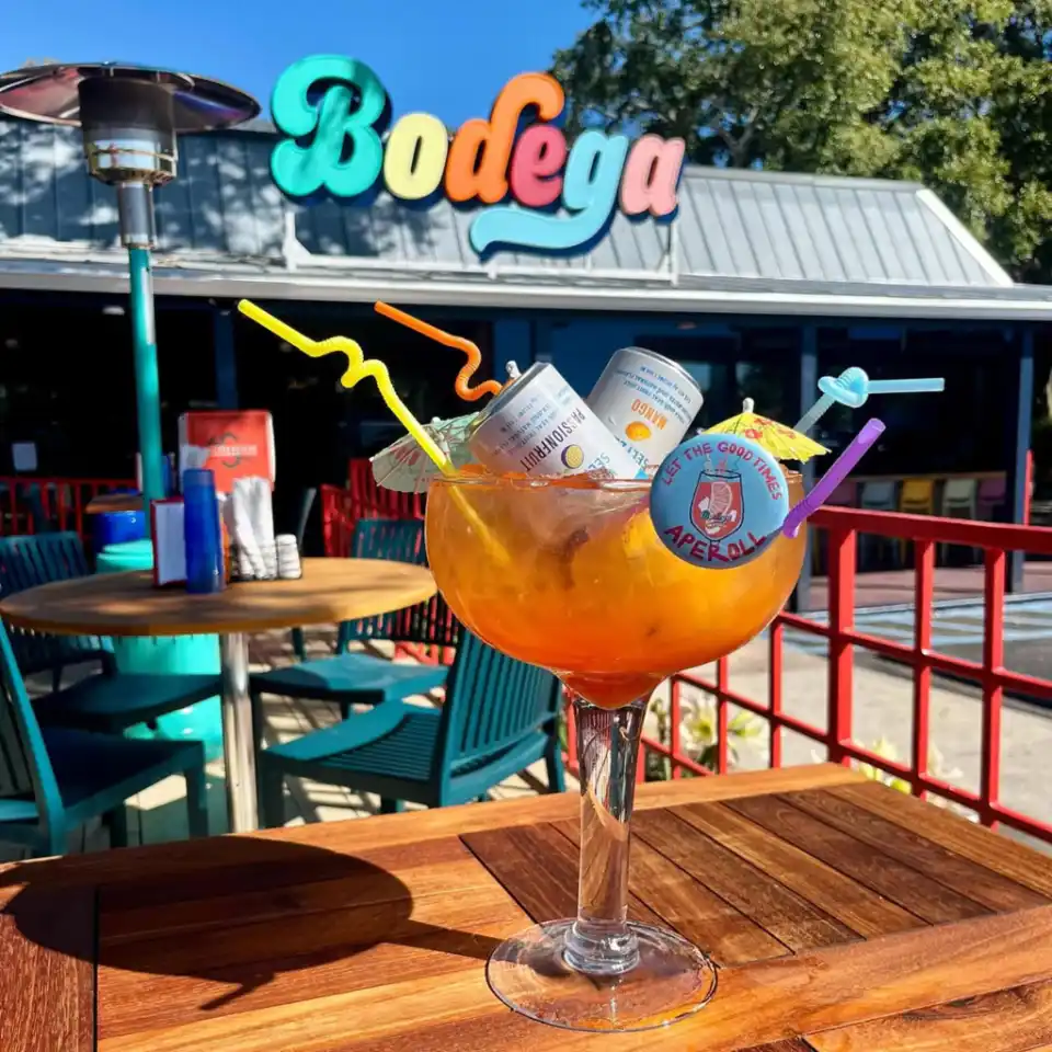 Large cocktail glass with straws and cans, outside a bodega under a colorful sign.