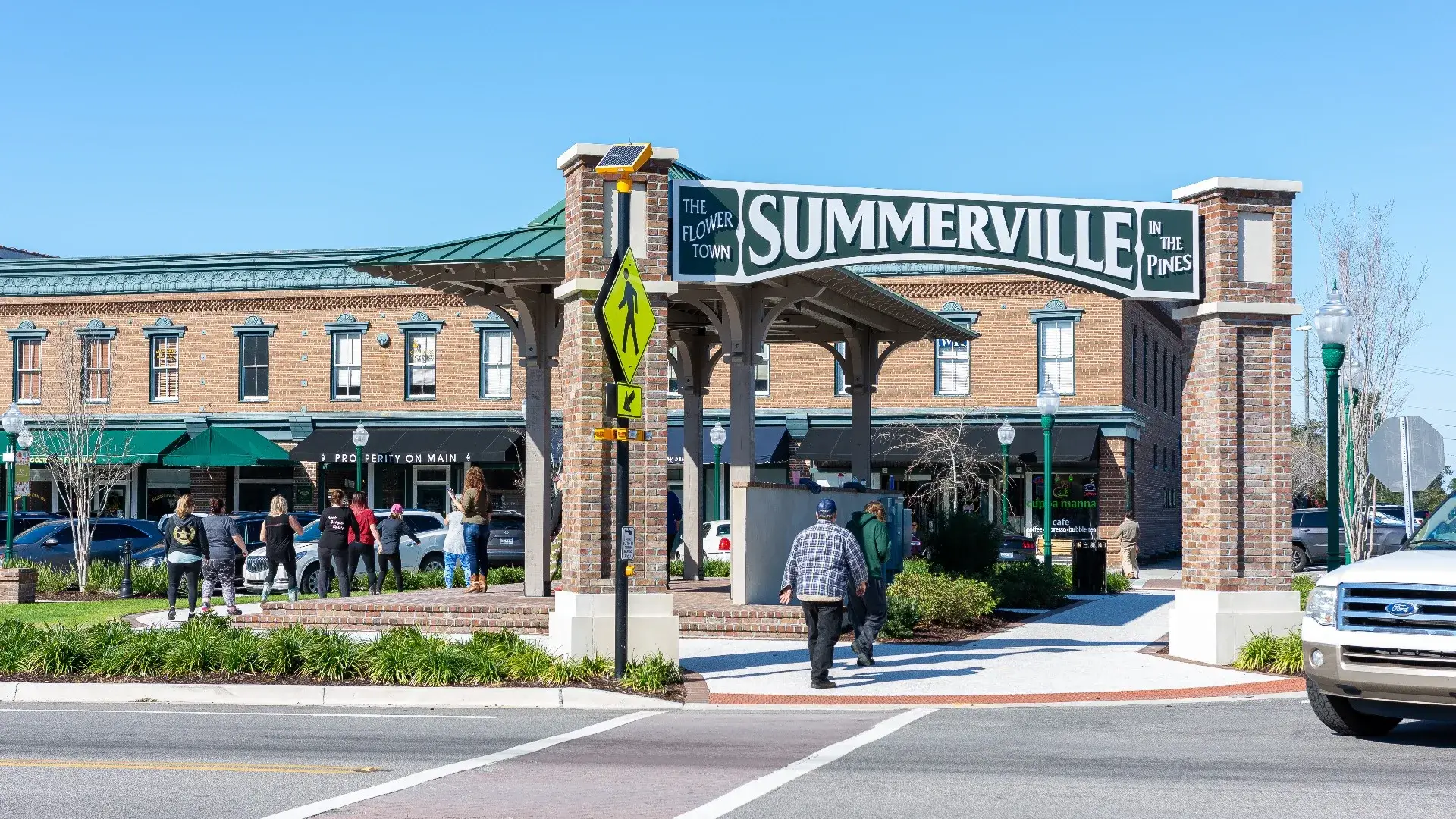 Large brick archway in Summerville, labeled "The Flower Town in the Pines," with people walking nearby and a brick building in the background.